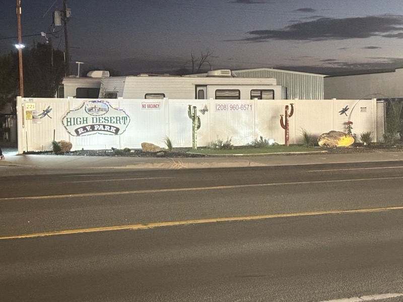 The High Desert RV Park sign and landscaped white fence lit up at dusk